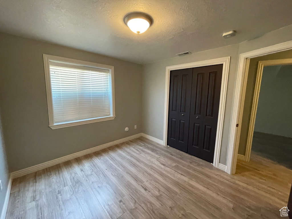 Unfurnished bedroom with a closet, light hardwood / wood-style floors, and a textured ceiling