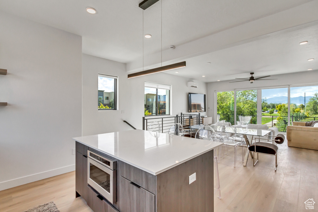 Kitchen with hanging light fixtures, a kitchen island, light hardwood / wood-style floors, and stainless steel microwave