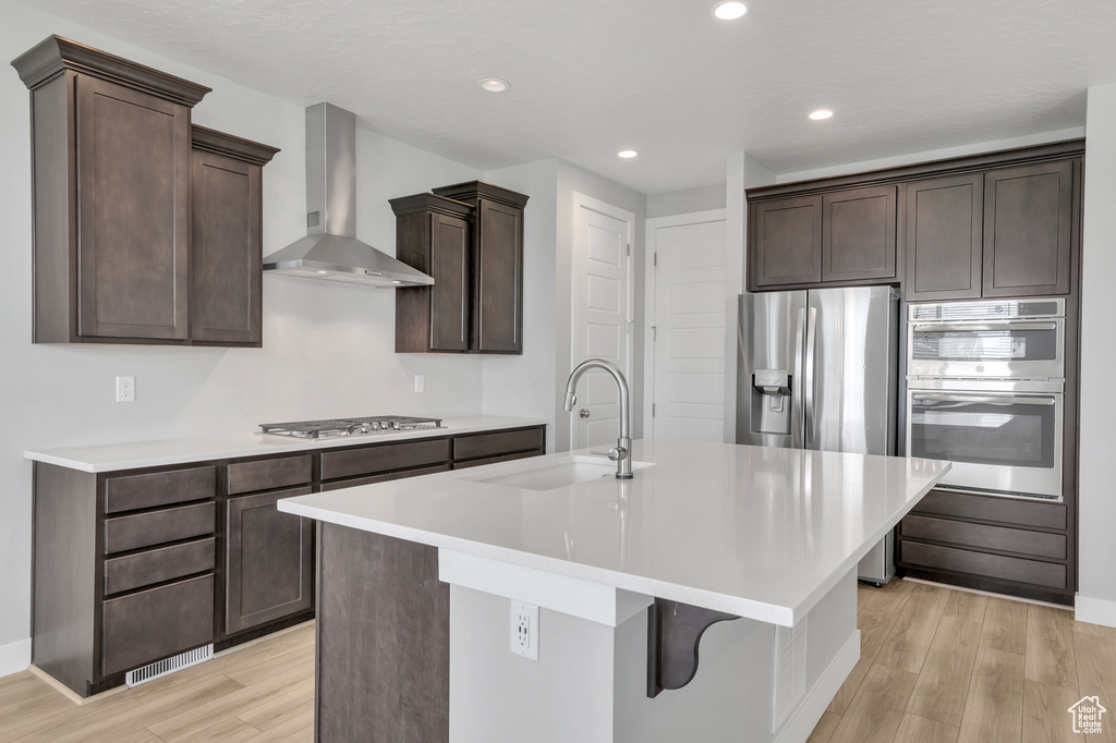 Kitchen with light hardwood / wood-style floors, a center island with sink, wall chimney exhaust hood, and sink