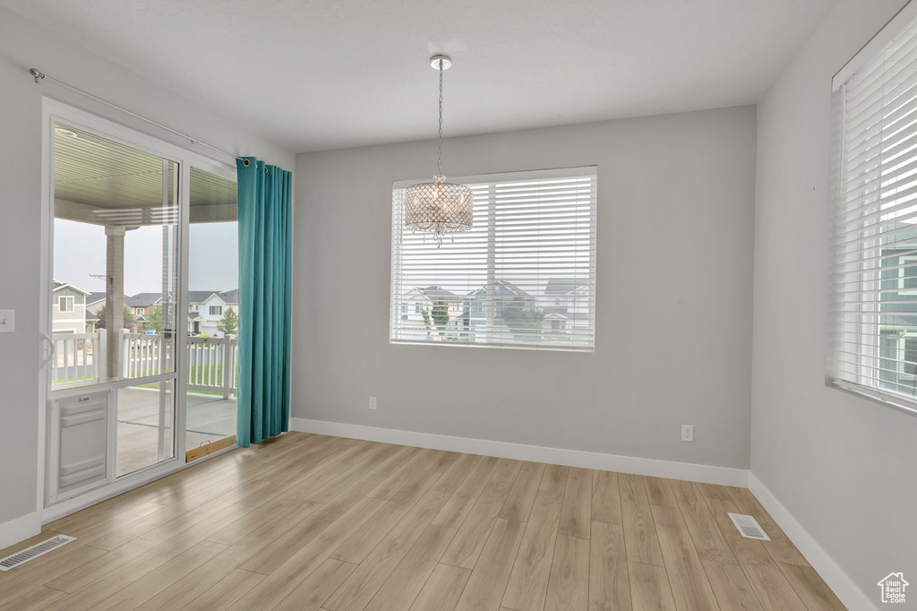 Unfurnished room with a healthy amount of sunlight, an inviting chandelier, and light hardwood / wood-style floors