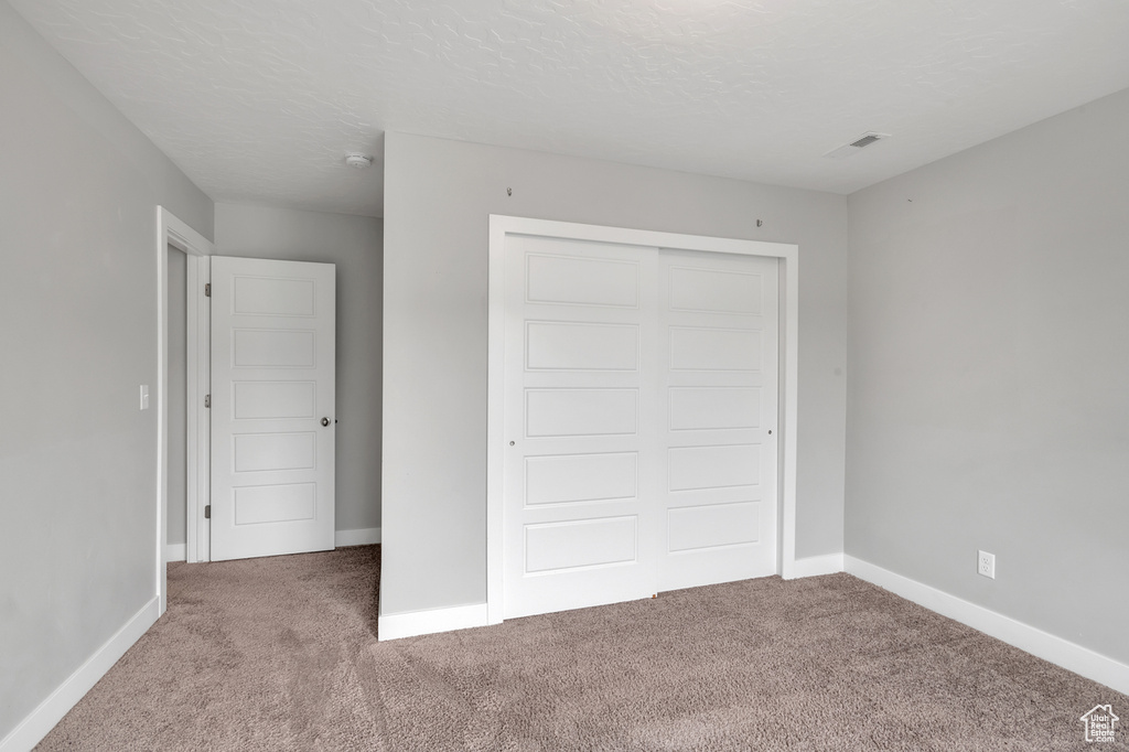 Unfurnished bedroom featuring a textured ceiling, carpet, and a closet