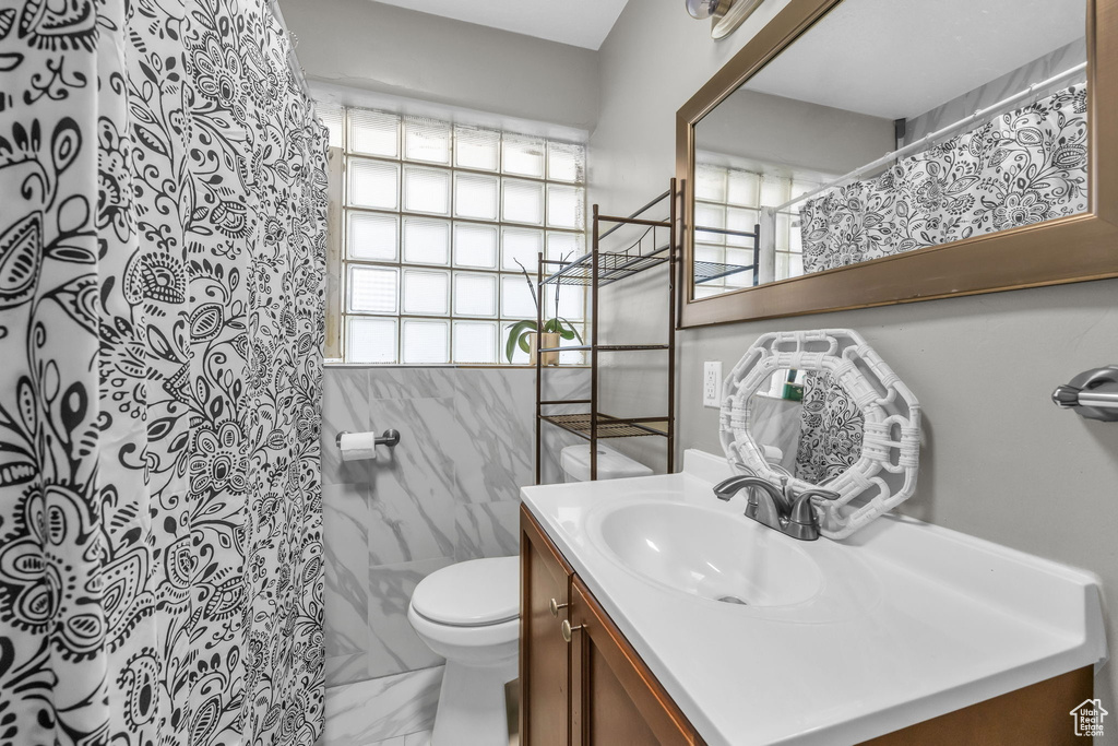 Bathroom with vanity, toilet, a shower with curtain, and tile walls