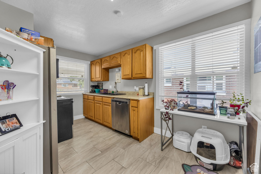 Kitchen featuring a textured ceiling, stainless steel dishwasher, and sink