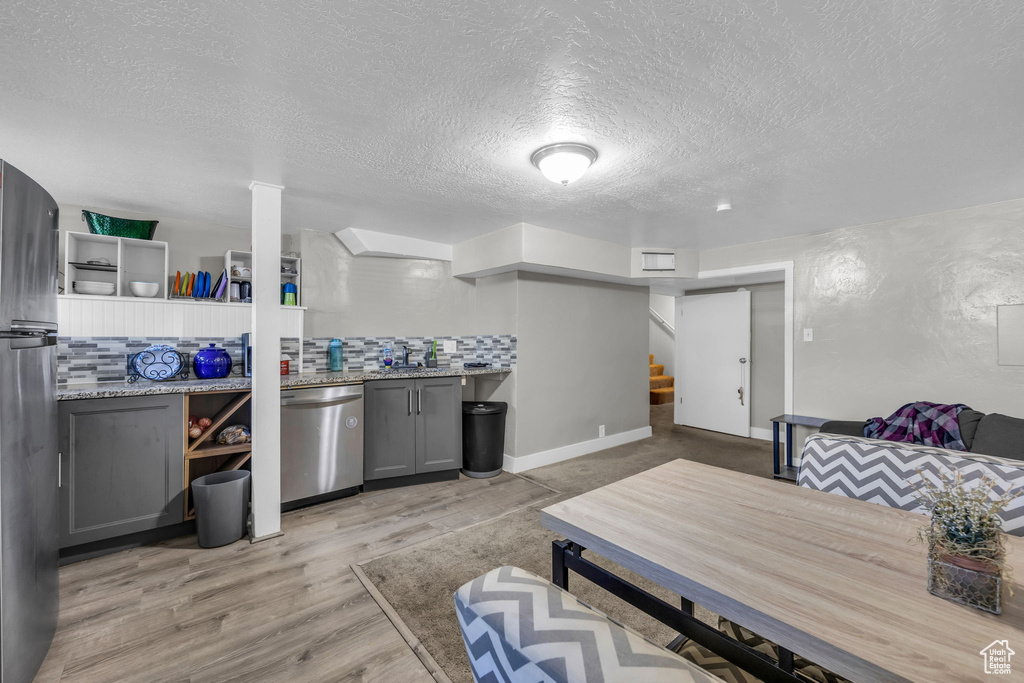 Kitchen featuring gray cabinetry, backsplash, light wood-type flooring, appliances with stainless steel finishes, and a textured ceiling