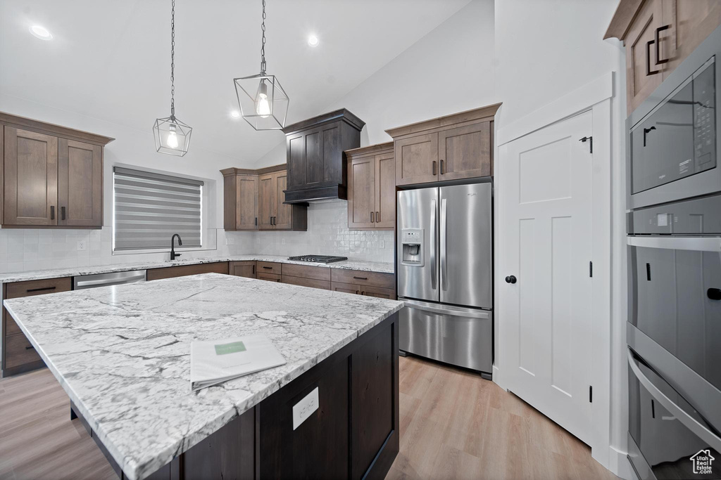 Kitchen with a kitchen island, decorative light fixtures, stainless steel appliances, lofted ceiling, and light wood-type flooring