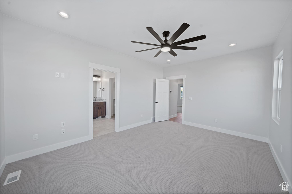 Unfurnished bedroom with light colored carpet, ceiling fan, and connected bathroom