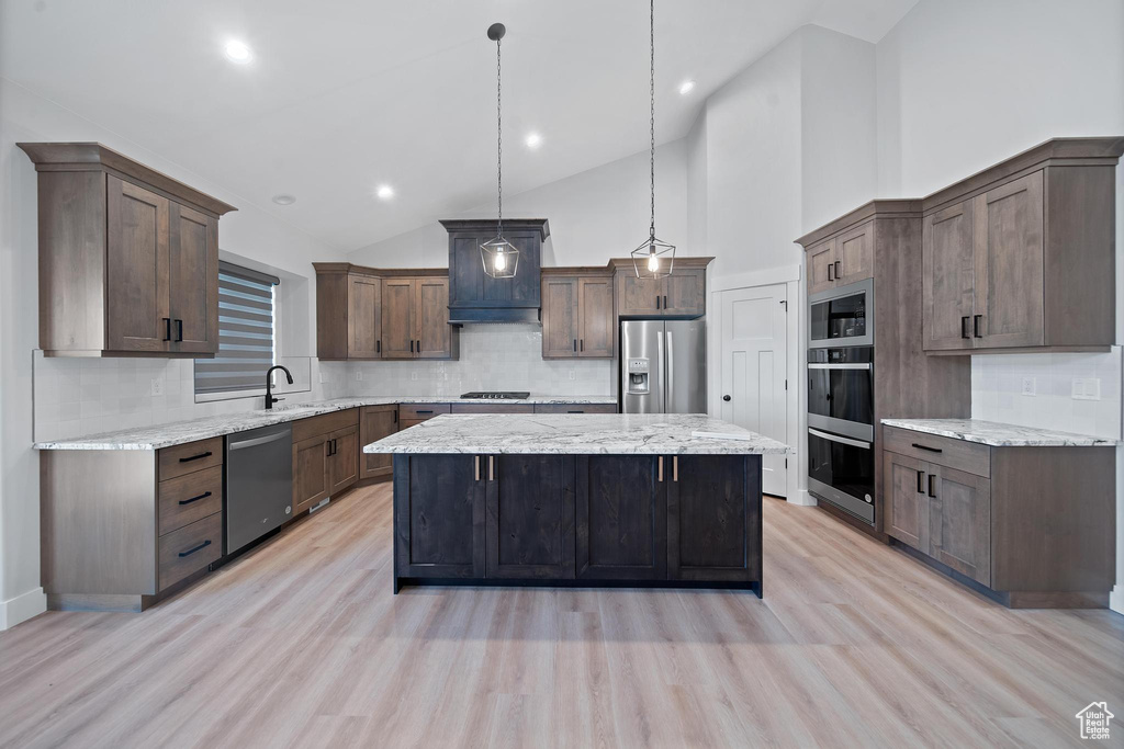 Kitchen with high vaulted ceiling, backsplash, decorative light fixtures, stainless steel appliances, and a center island