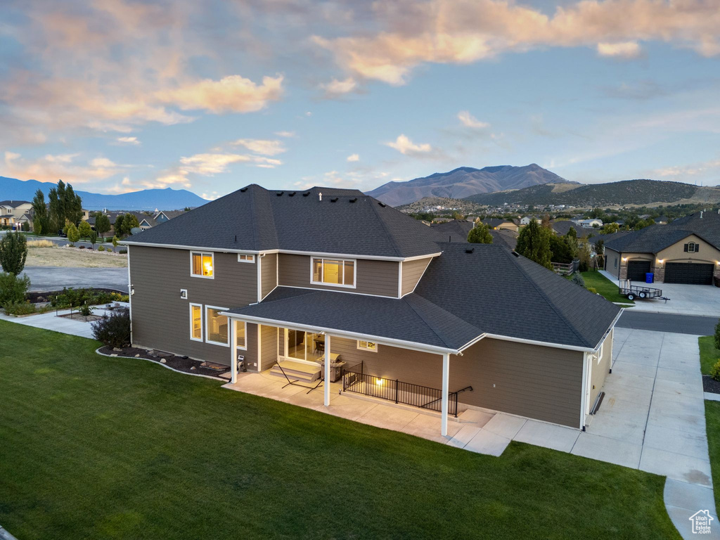 Back house at dusk with a mountain view, a lawn, a garage, and an outbuilding