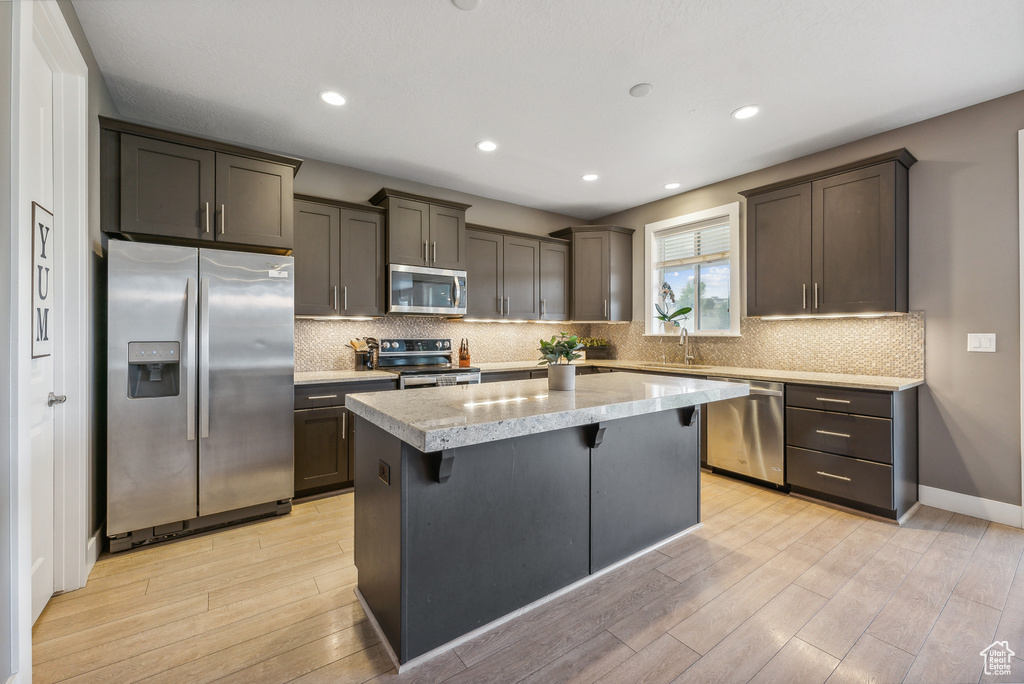 Kitchen with a kitchen island, light hardwood / wood-style flooring, a breakfast bar, stainless steel appliances, and sink