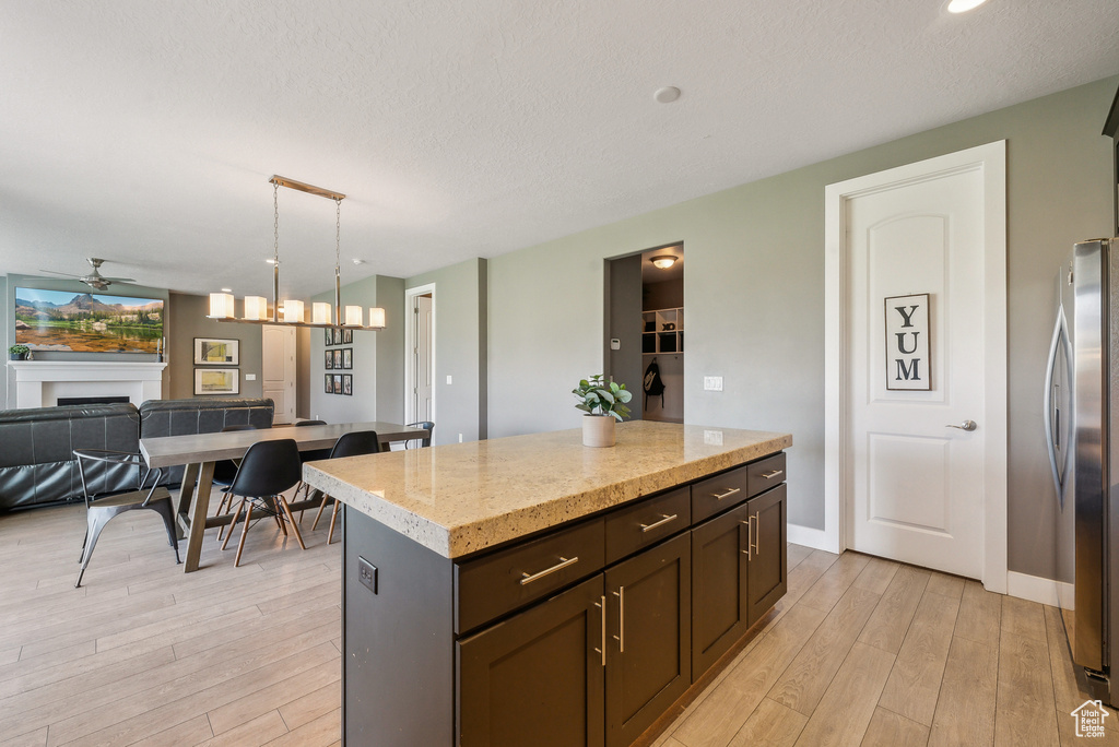 Kitchen with stainless steel fridge, decorative light fixtures, a center island, ceiling fan, and light hardwood / wood-style floors