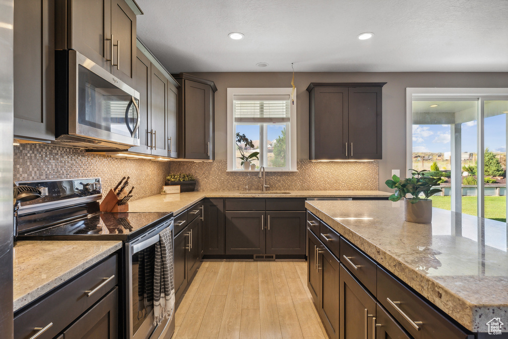 Kitchen with dark brown cabinets, stainless steel appliances, sink, decorative backsplash, and light hardwood / wood-style floors