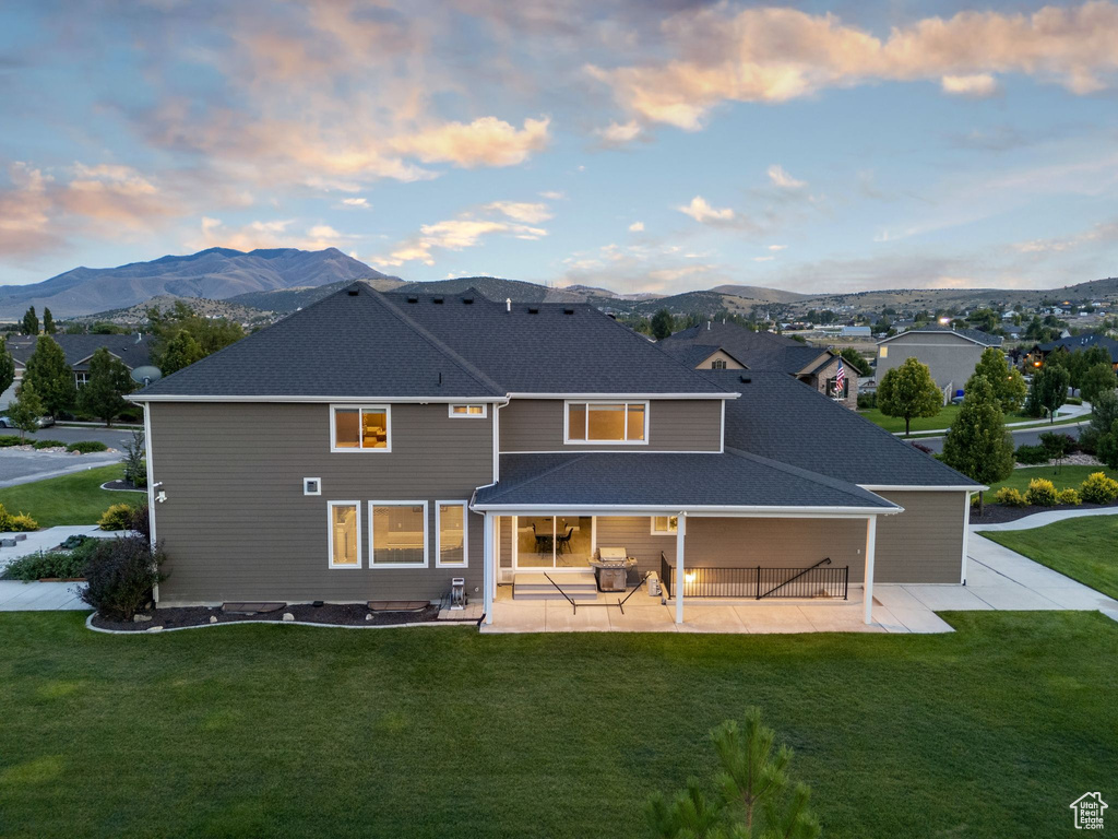 Back house at dusk featuring a mountain view, a yard, and a patio