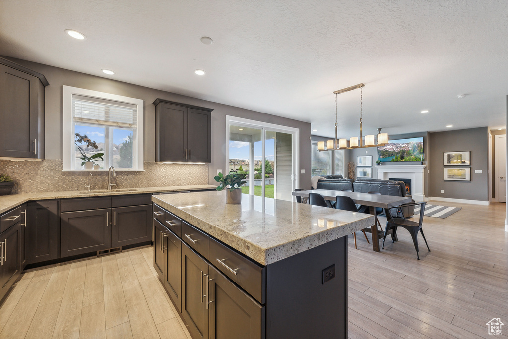 Kitchen with backsplash, a center island, light hardwood / wood-style flooring, light stone counters, and sink