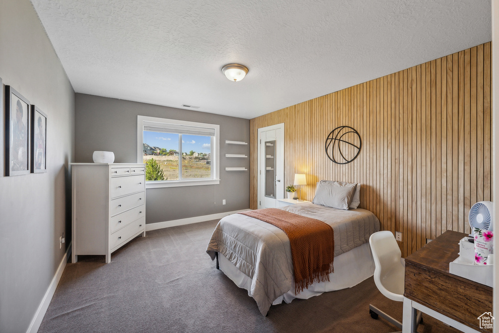 Carpeted bedroom featuring wooden walls and a textured ceiling