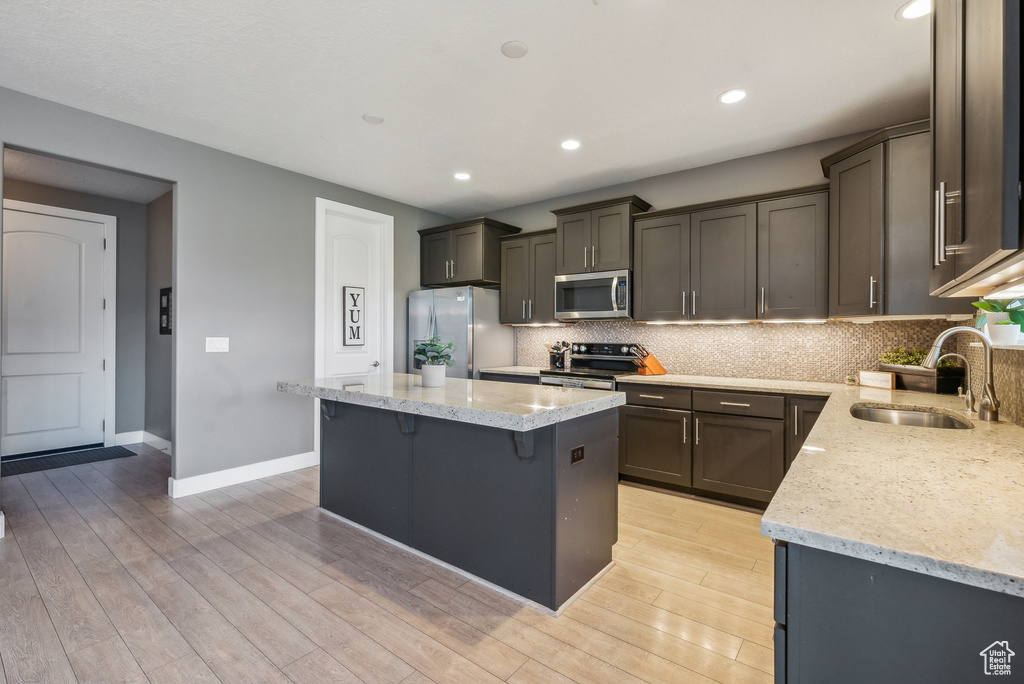 Kitchen featuring a center island, light stone counters, stainless steel appliances, light hardwood / wood-style floors, and sink