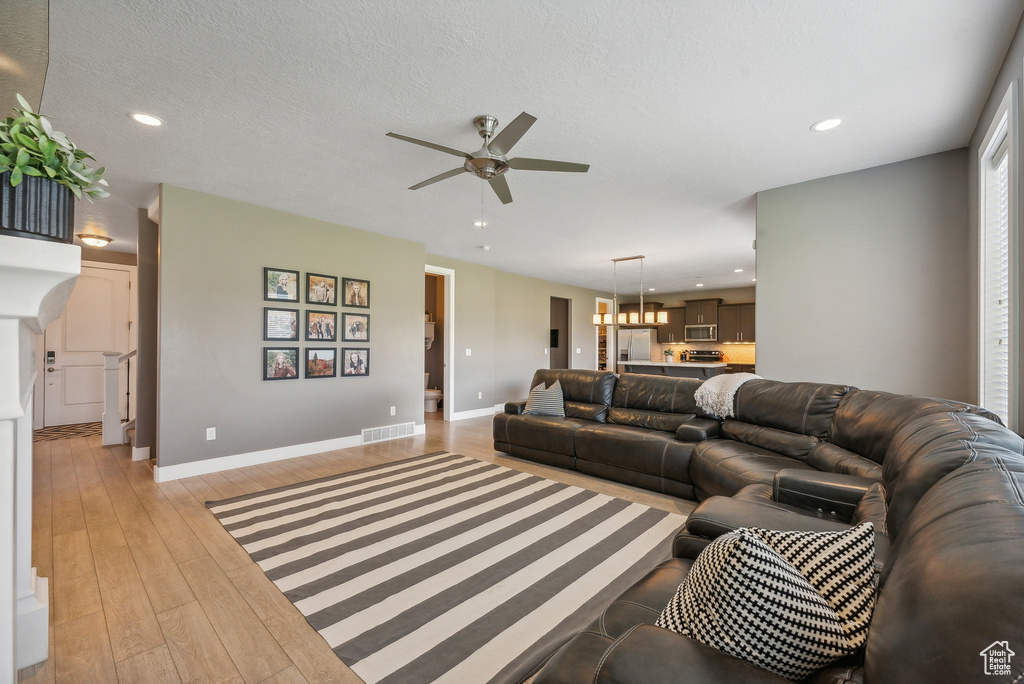 Living room featuring ceiling fan with notable chandelier, a textured ceiling, and light hardwood / wood-style flooring