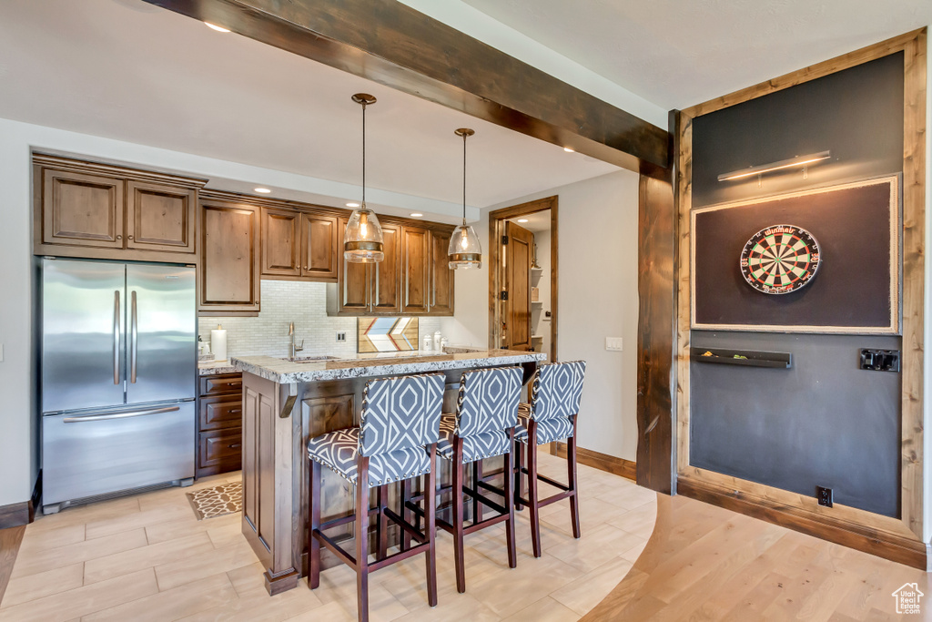 Kitchen featuring a breakfast bar area, stainless steel built in fridge, light hardwood / wood-style flooring, hanging light fixtures, and light stone counters