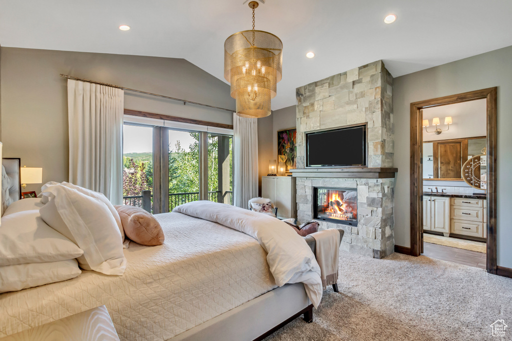 Carpeted bedroom featuring lofted ceiling, connected bathroom, an inviting chandelier, and a stone fireplace