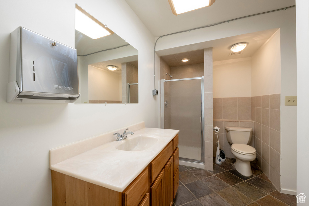 Bathroom with toilet, tile patterned floors, vanity, tile walls, and a shower with shower door