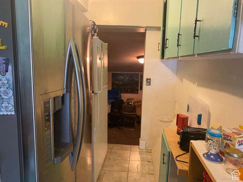 Kitchen with light tile patterned flooring, green cabinetry, and stainless steel refrigerator with ice dispenser