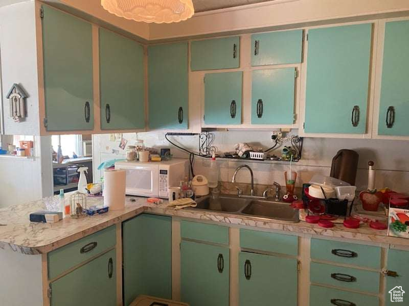 Kitchen featuring green cabinets, backsplash, kitchen peninsula, and sink