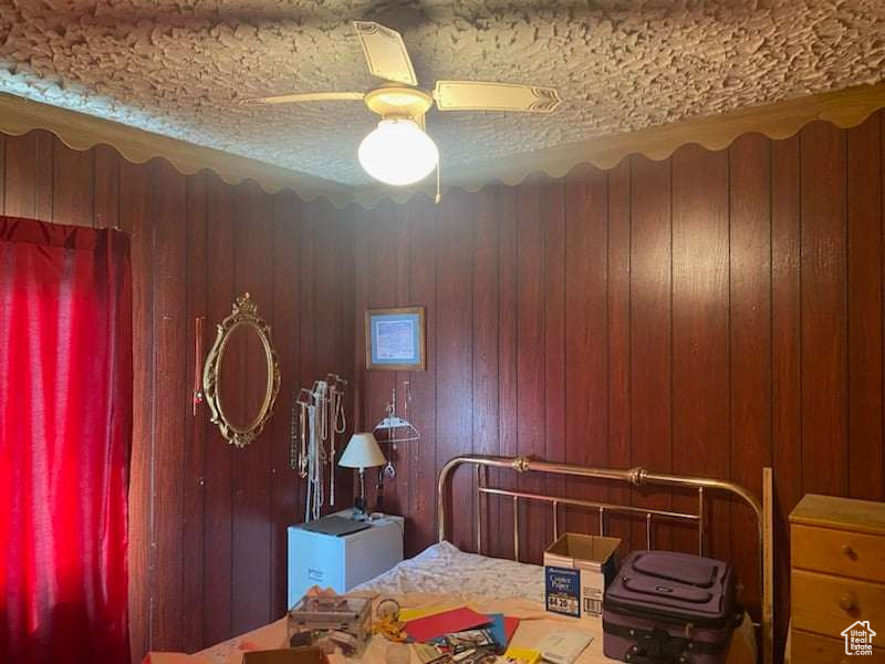 Bedroom featuring a textured ceiling, ceiling fan, and wood walls