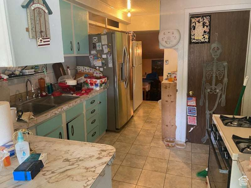 Kitchen with white range with gas cooktop, stainless steel fridge with ice dispenser, sink, green cabinetry, and light tile patterned flooring