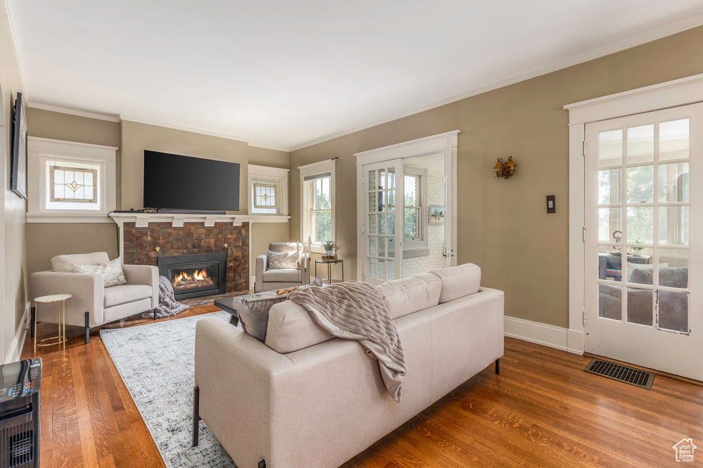 Living room featuring a healthy amount of sunlight, a tiled fireplace, dark wood-type flooring, and crown molding