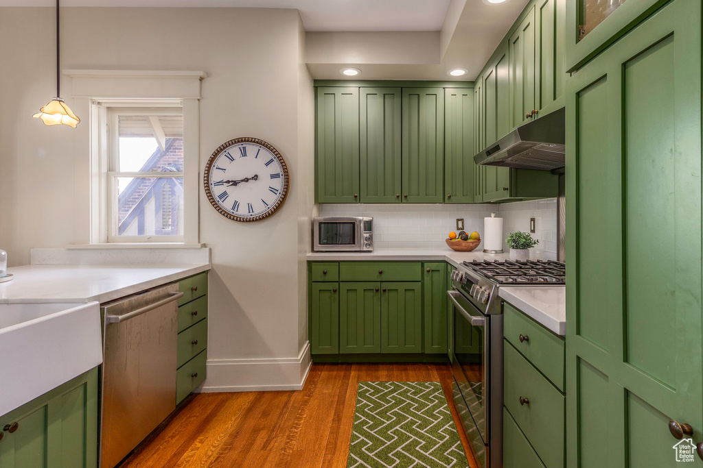 Kitchen with hanging light fixtures, tasteful backsplash, wood-type flooring, green cabinetry, and appliances with stainless steel finishes