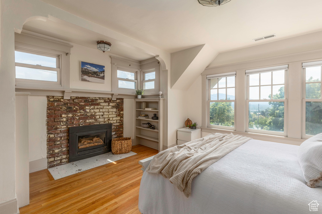 Bedroom featuring a brick fireplace, light hardwood / wood-style flooring, and multiple windows