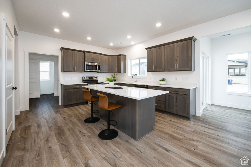 Kitchen with dark brown cabinets, a kitchen bar, light countertops, appliances with stainless steel finishes, and a kitchen island