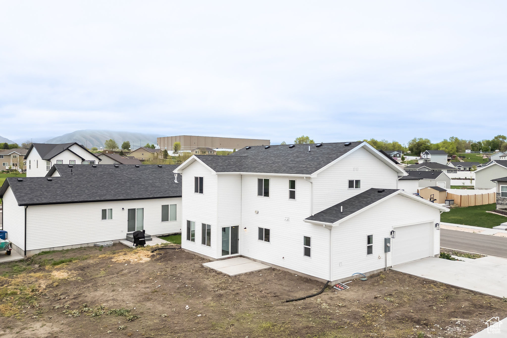 Rear view of house featuring driveway, a garage, a shingled roof, and a residential view