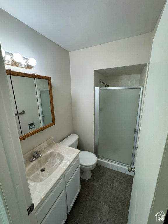 Bathroom featuring a shower with door, vanity, toilet, and tile patterned floors