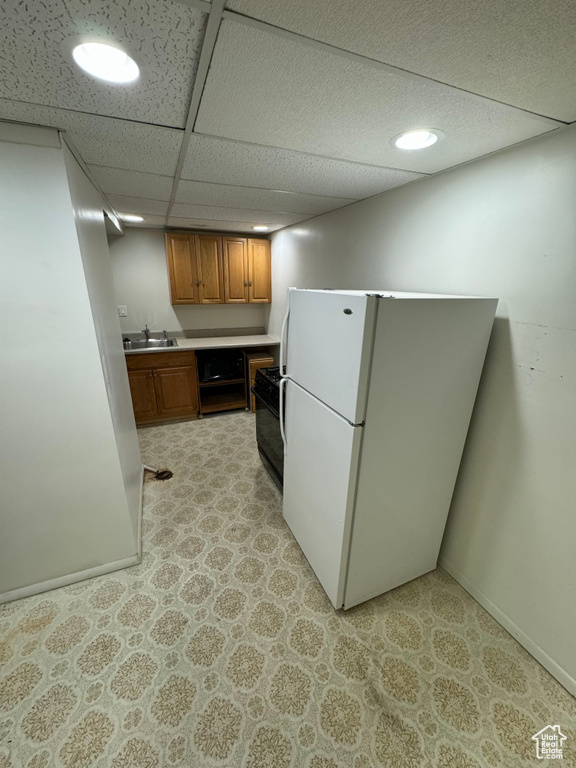 Kitchen featuring black range with electric cooktop, a paneled ceiling, sink, and white refrigerator