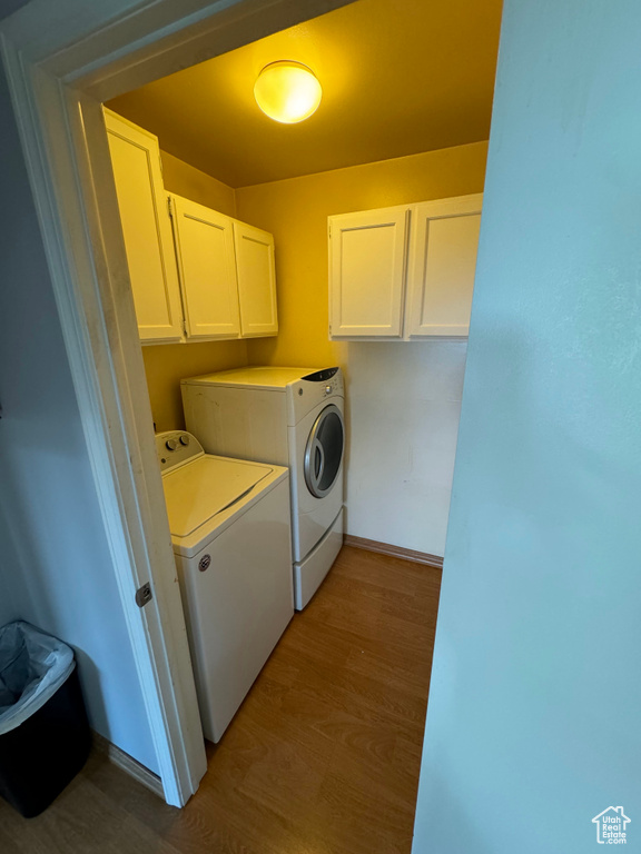 Clothes washing area with cabinets, washer and dryer, and light hardwood / wood-style floors