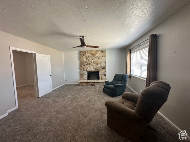 Carpeted living room featuring a fireplace, a textured ceiling, and ceiling fan