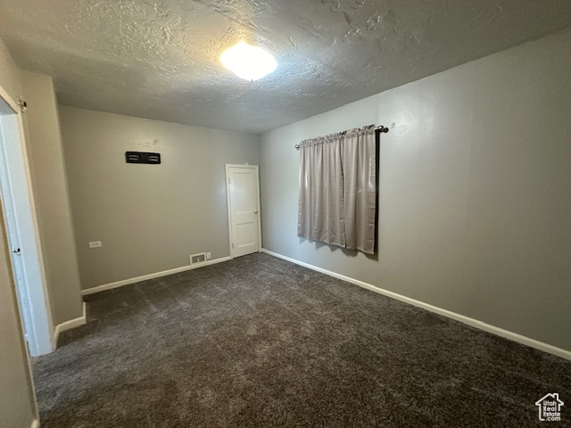 Spare room featuring a textured ceiling and dark colored carpet