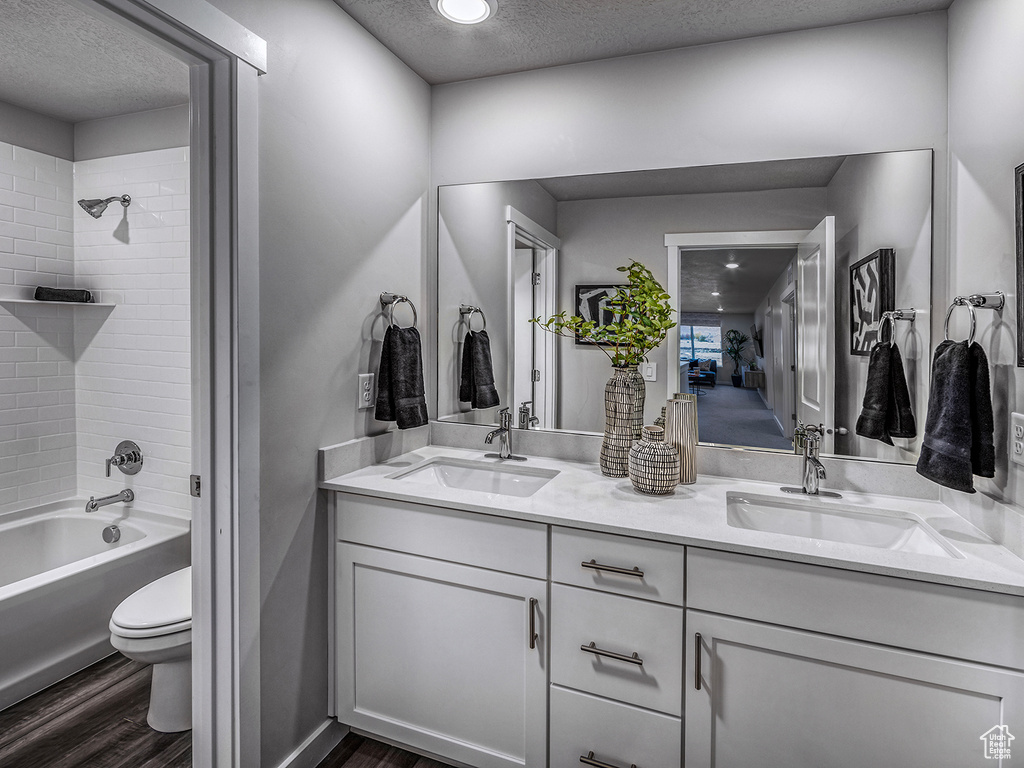 Full bathroom featuring toilet, vanity, a textured ceiling, tiled shower / bath combo, and hardwood / wood-style flooring