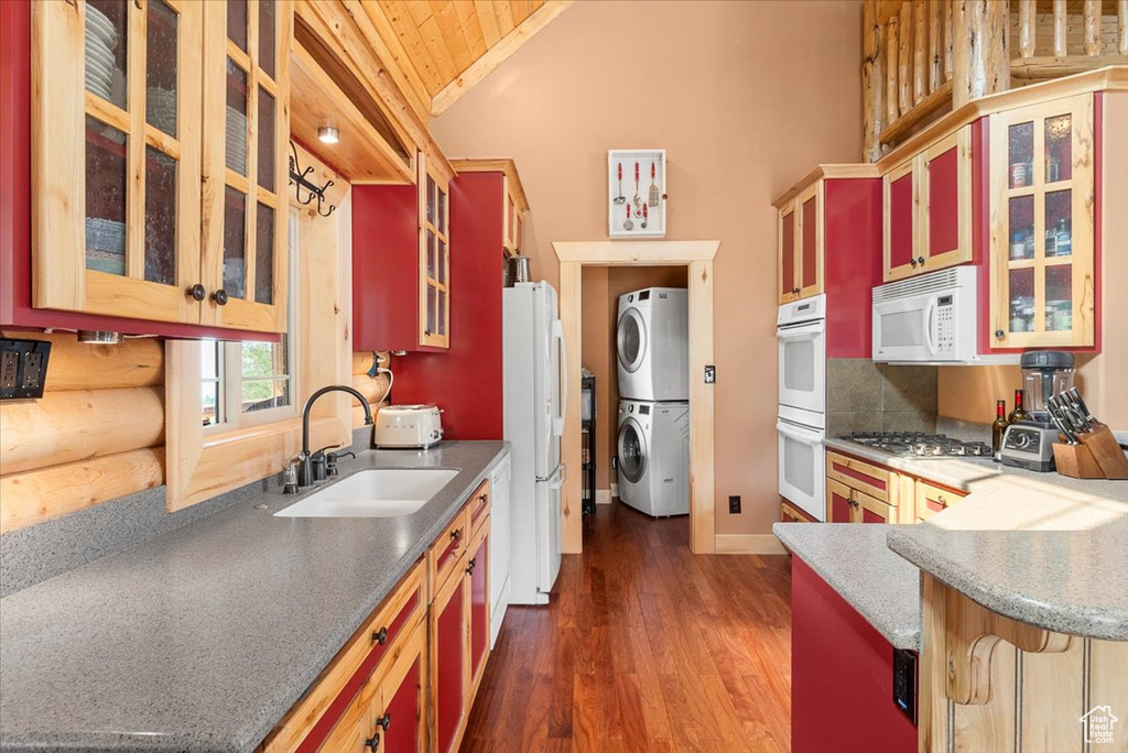 Kitchen featuring white appliances, sink, stacked washer / dryer, dark hardwood / wood-style floors, and decorative backsplash