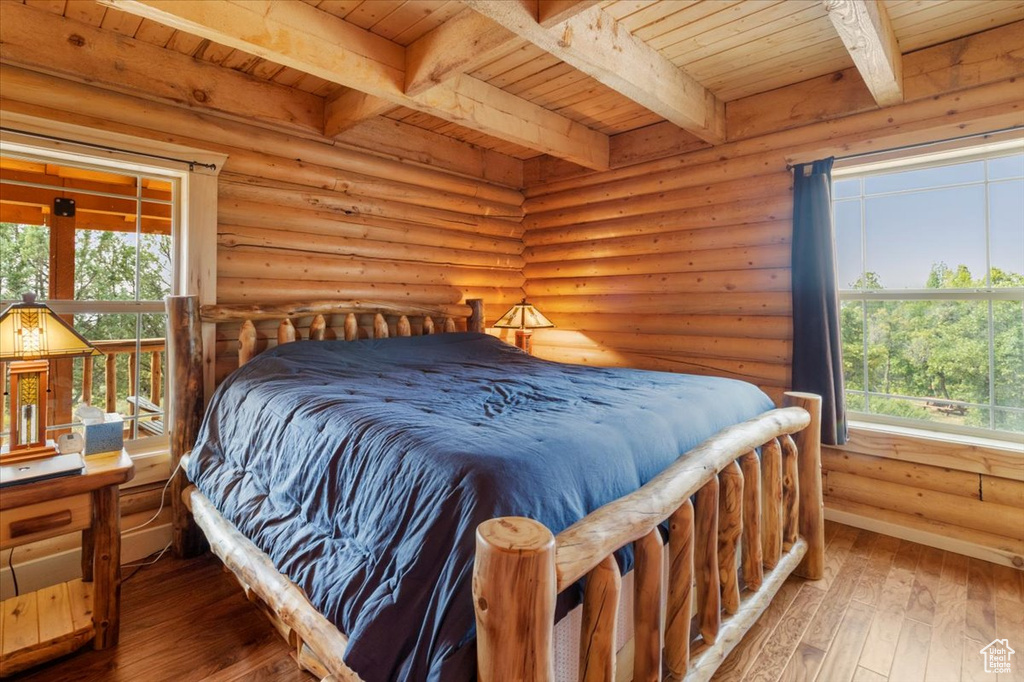 Bedroom with wooden ceiling, beamed ceiling, hardwood / wood-style floors, and rustic walls