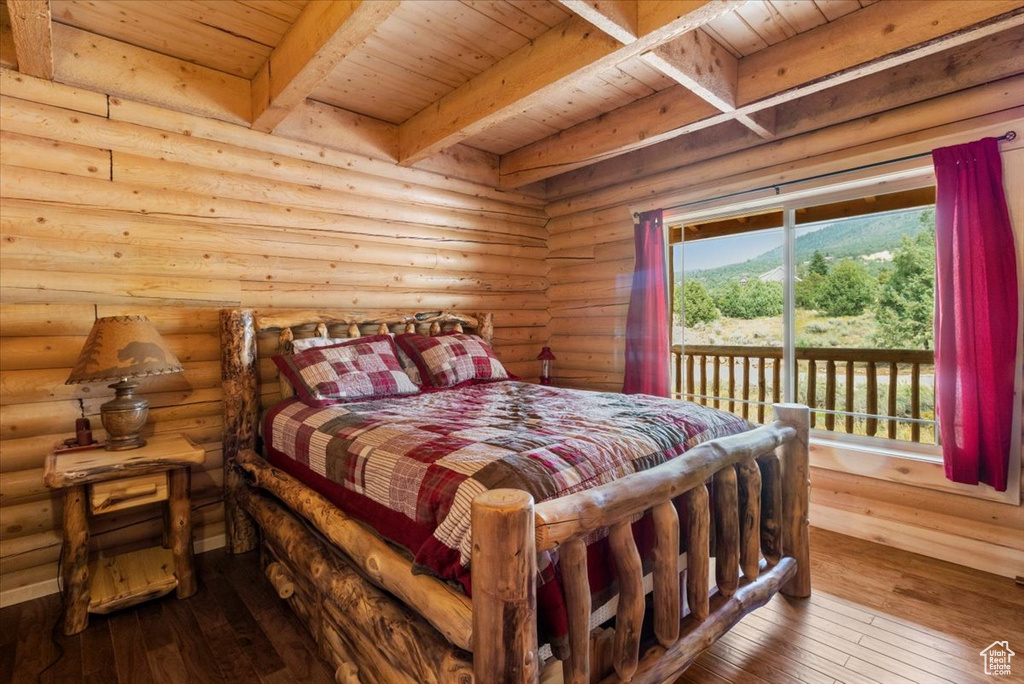 Bedroom with log walls, wooden ceiling, hardwood / wood-style floors, beam ceiling, and access to exterior