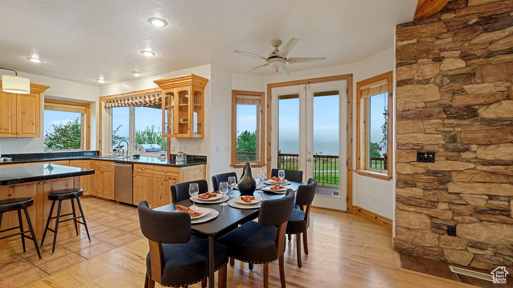 Dining room featuring a water view, a textured ceiling, light hardwood / wood-style flooring, ceiling fan, and french doors