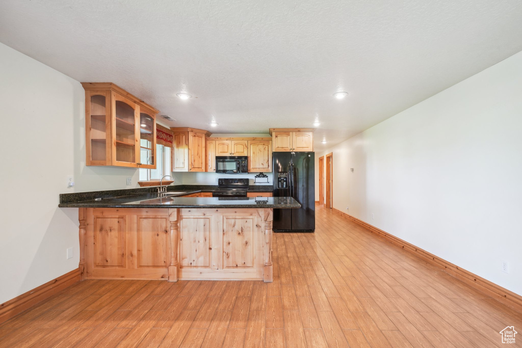 Kitchen with a breakfast bar area, black appliances, light hardwood / wood-style floors, kitchen peninsula, and sink