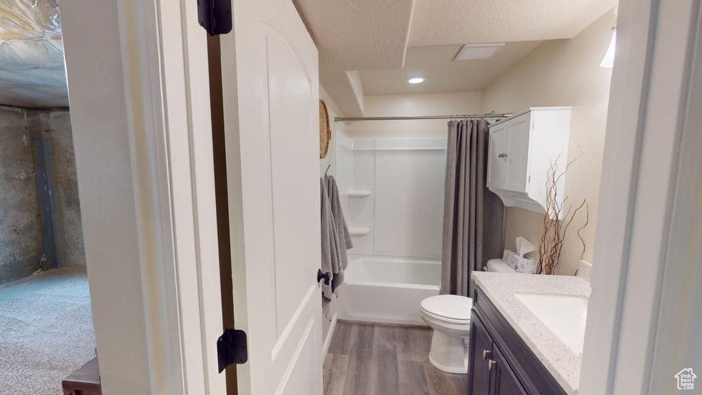 Full bathroom featuring hardwood / wood-style flooring, toilet, shower / bath combination with curtain, vanity, and a textured ceiling