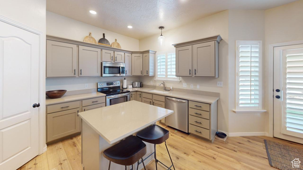 Kitchen with light wood-type flooring, appliances with stainless steel finishes, gray cabinetry, and hanging light fixtures