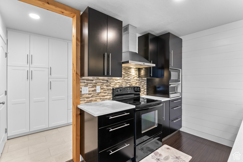 Kitchen featuring light tile patterned floors, black appliances, decorative backsplash, wall chimney exhaust hood, and white cabinets