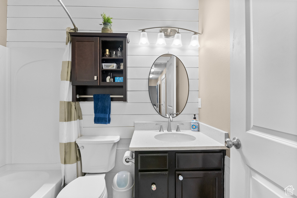 Full bathroom with shower / bath combination with curtain, toilet, wooden walls, and vanity