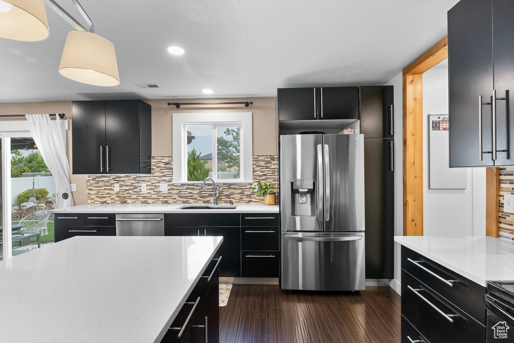 Kitchen with dark hardwood / wood-style floors, pendant lighting, stainless steel appliances, sink, and decorative backsplash