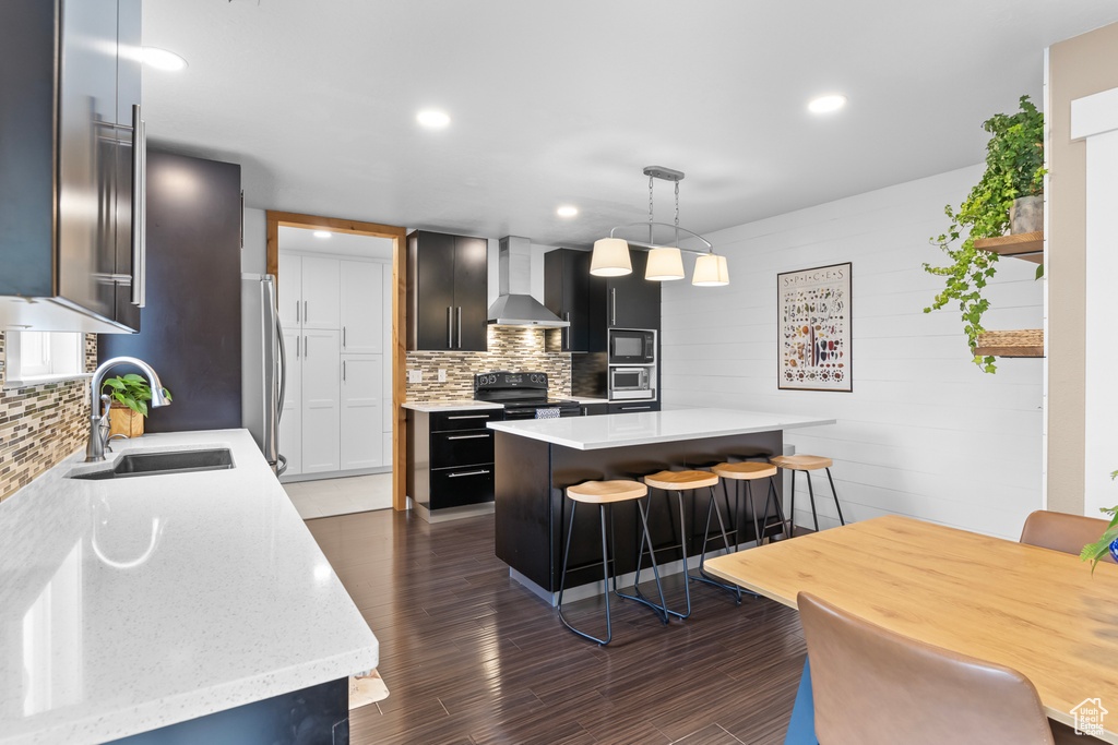 Kitchen featuring sink, dark hardwood / wood-style floors, wall chimney exhaust hood, pendant lighting, and a kitchen island