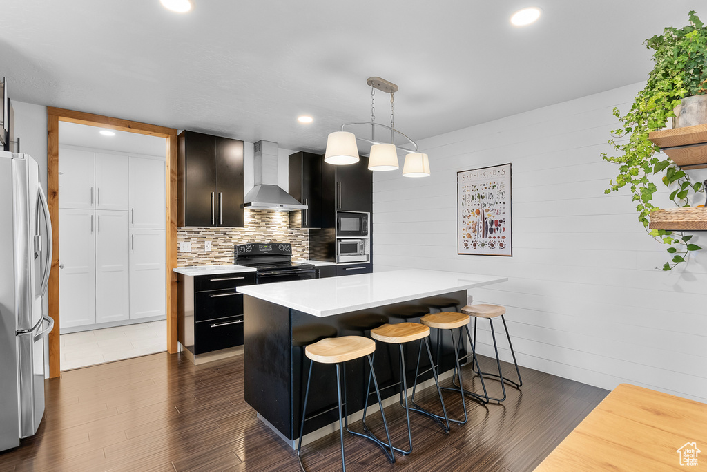 Kitchen featuring hanging light fixtures, black appliances, dark hardwood / wood-style floors, wall chimney exhaust hood, and a kitchen island